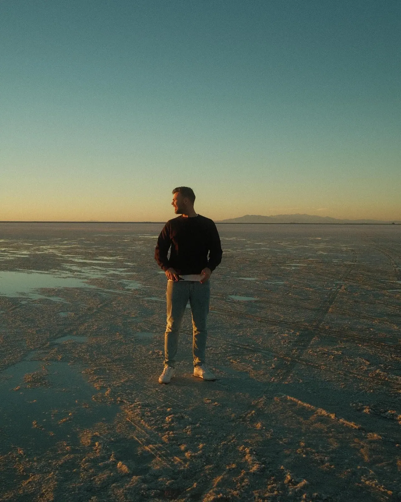Tommy Jackett standing alone on the Bonneville Salt Flats at dusk, with wet salt stretching to the horizon.